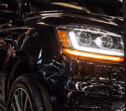 Close-up of the front left side of a black car showing the headlight with LED accents and part of the fender and wheel.