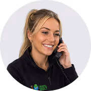 Smiling woman with blonde hair talking on a phone against a light background.