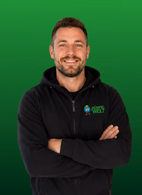 Smiling man with crossed arms wearing a black Rumpel Welt hoodie on a green background.