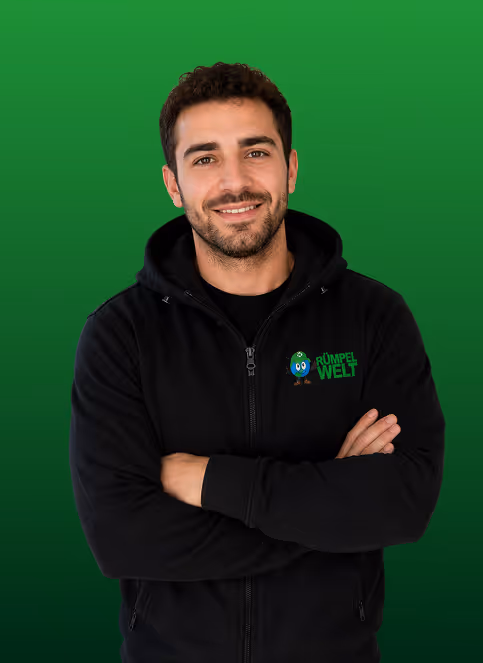 Smiling man in black hoodie with RÜMPEL WELT logo on green gradient background.