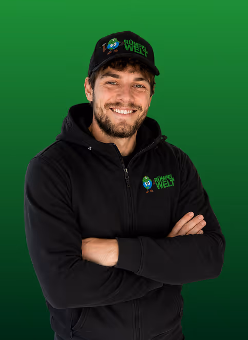 Smiling man wearing black cap and hoodie with Rümpel Welt logo on green background.