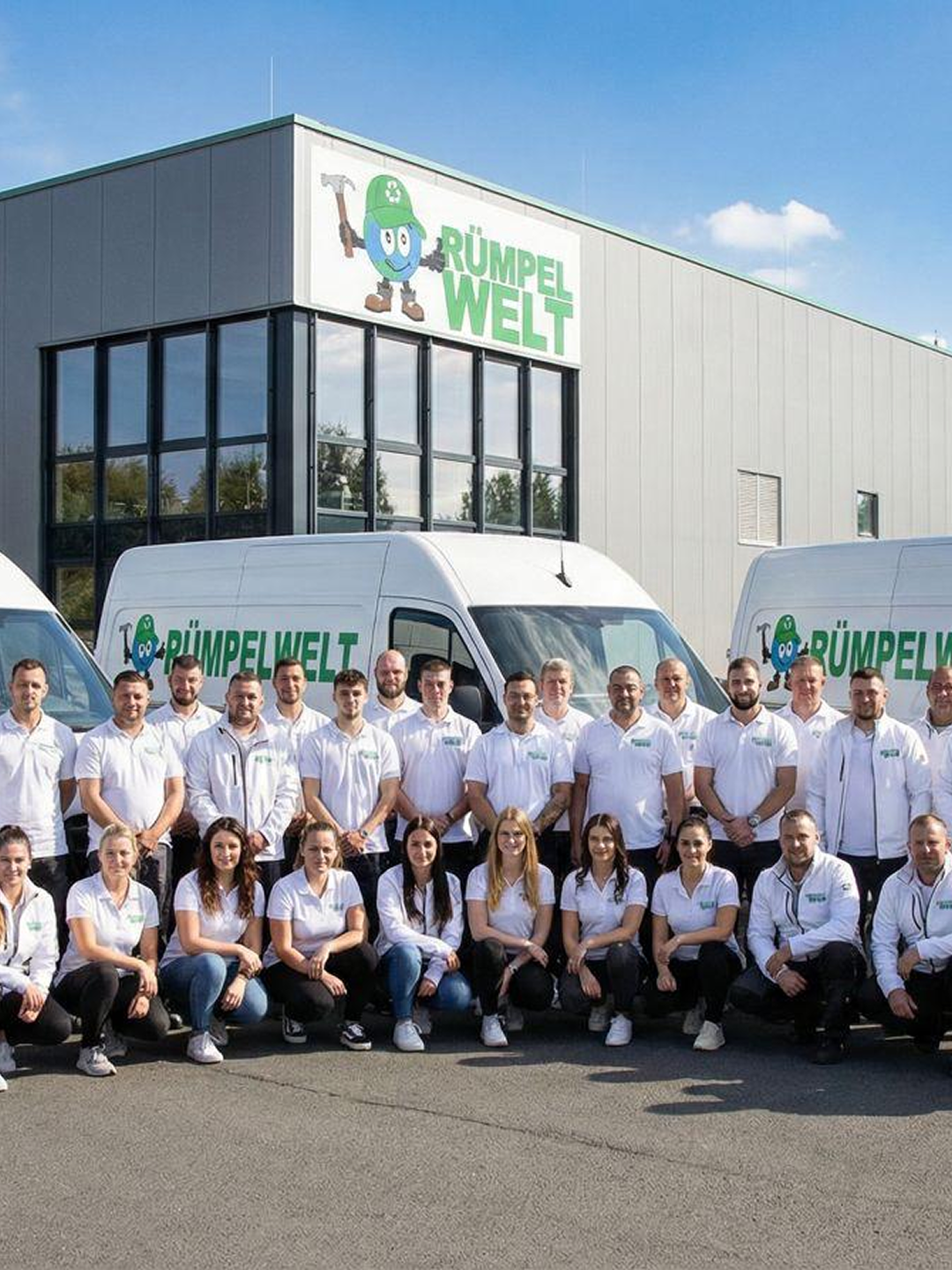 Group of diverse employees in white shirts posing outdoors by company vans and building under clear sky.
