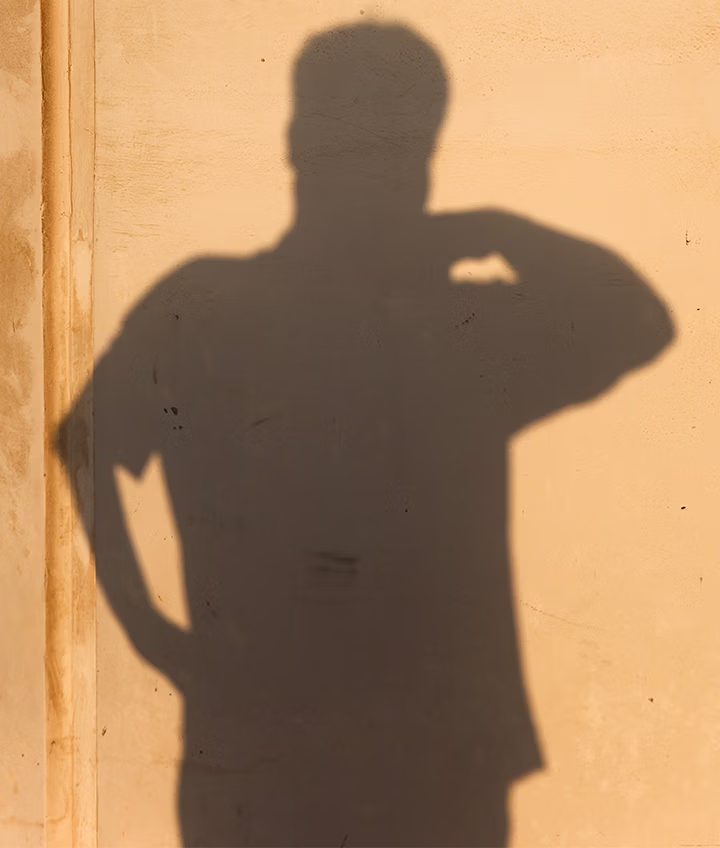 Shadow of a person with one hand on hip and the other bent near the head on a beige wall.