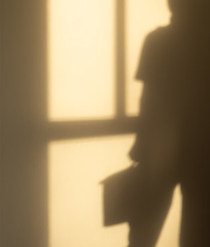 Shadow of person holding a folder or briefcase cast on a wall with window light.