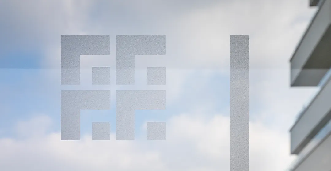Dettaglio di una vetrata con elemento grafico geometrico e architettura contemporanea sullo sfondo.
