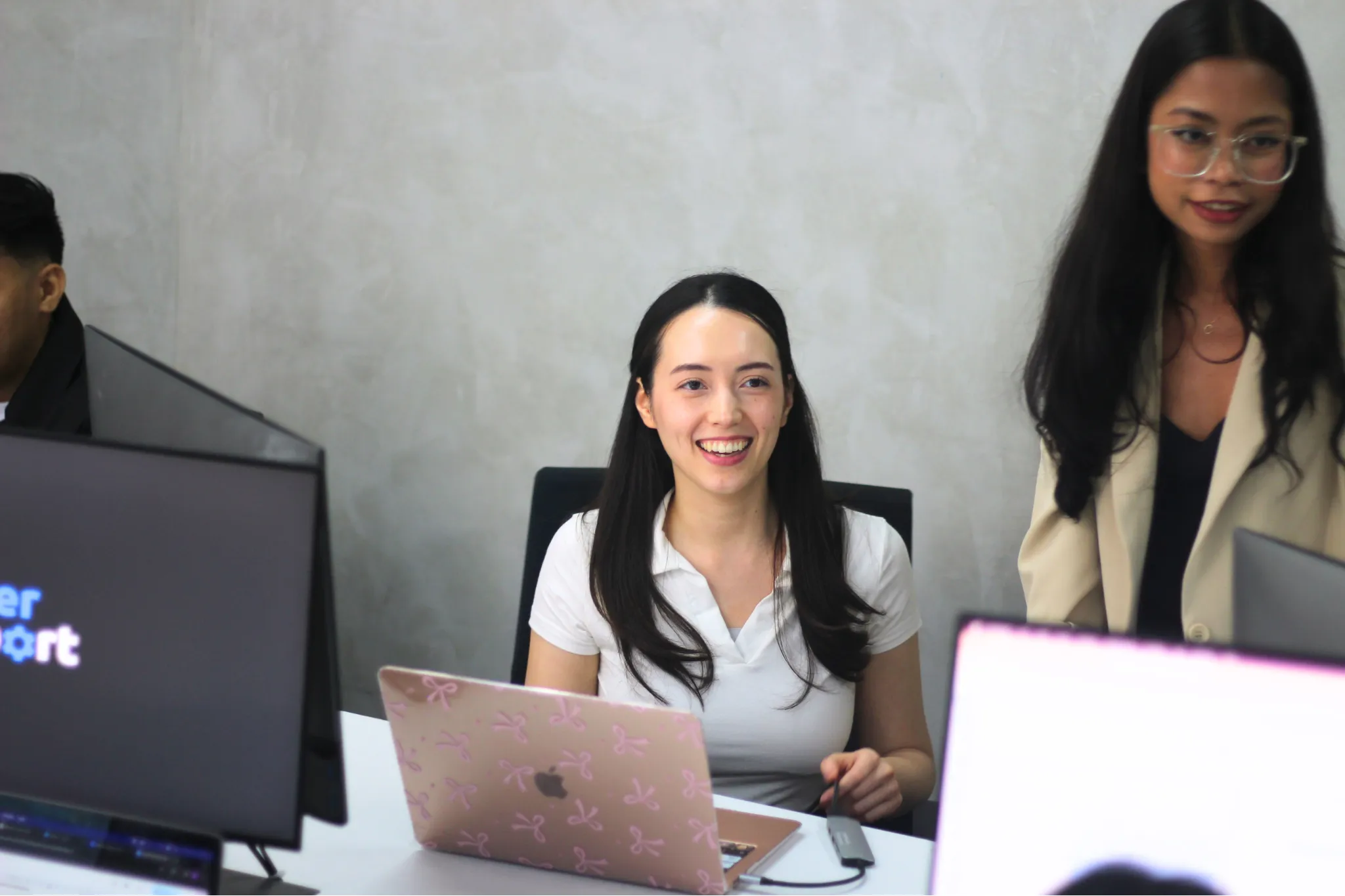 Two women working at desks with laptops and monitors in an office setting.