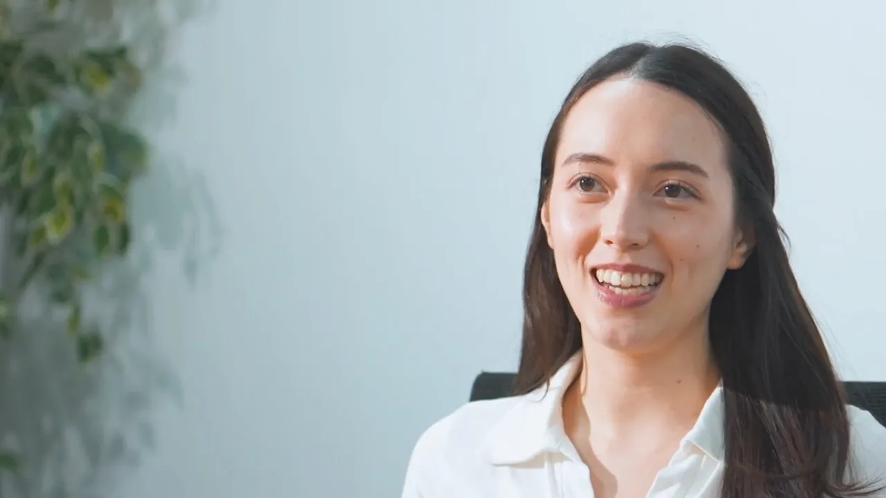 Smiling woman with long dark hair wearing a white shirt against a light background.
