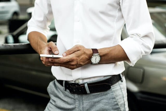 Mann mit Smartphone vor Auto