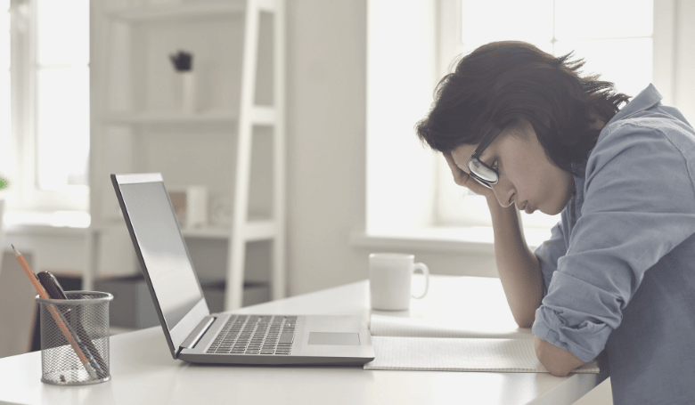 Person sitzt frustriert vor einem Blatt und Laptop