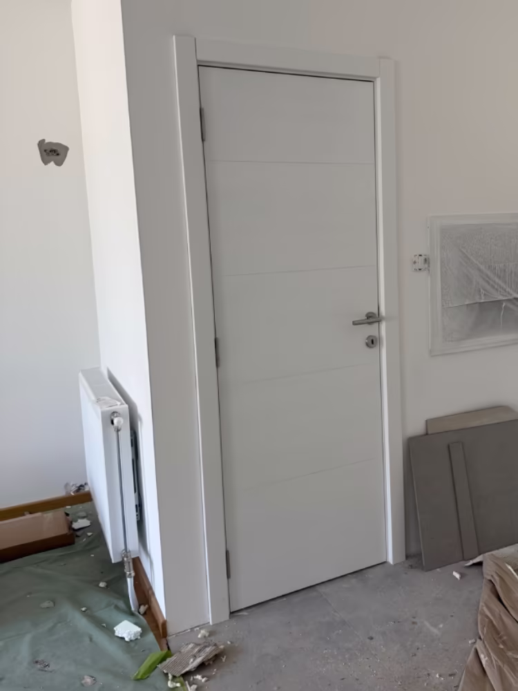 Unutrašnja bela vrata sa metalnom kvakom u prostoriji u fazi renoviranja.