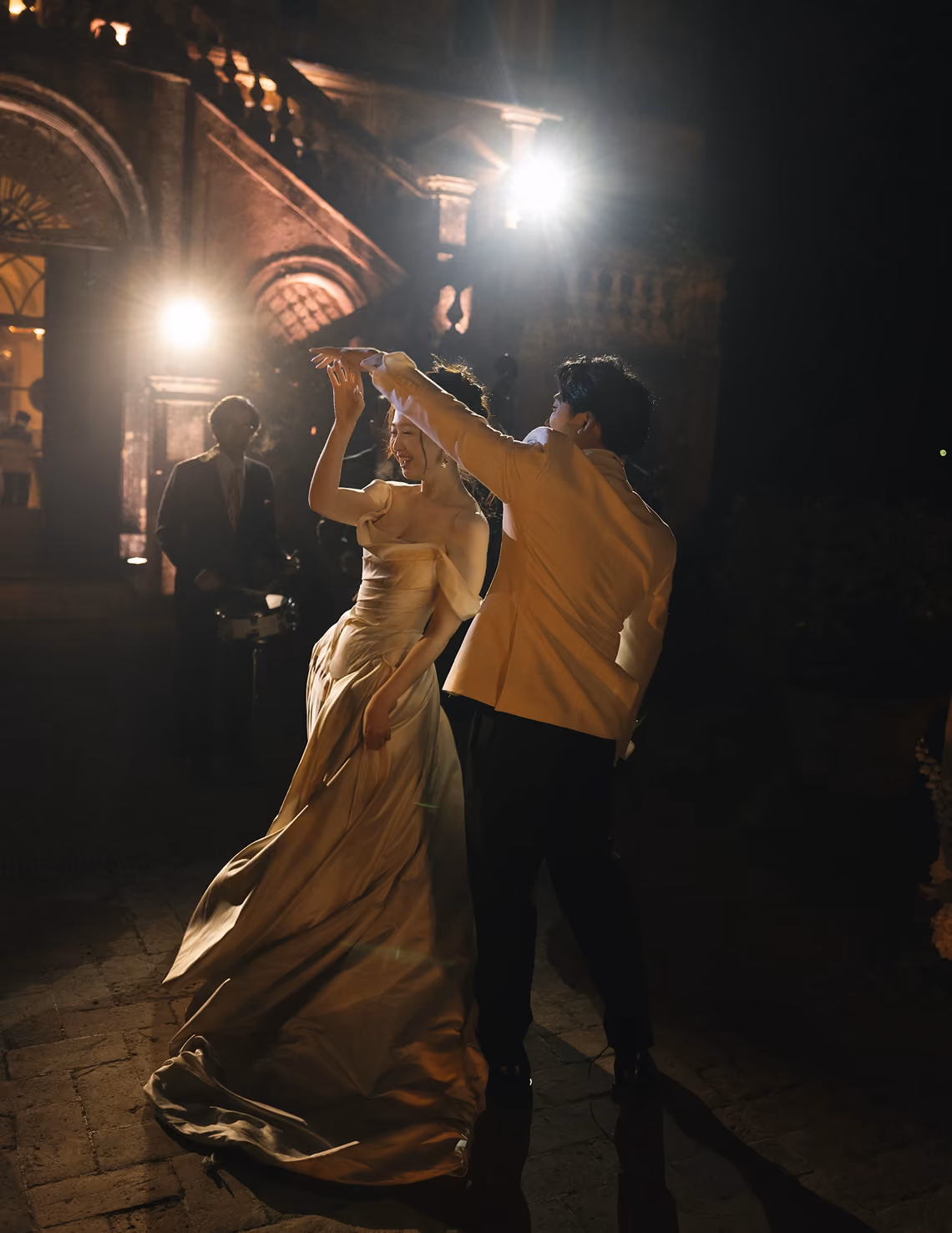 Couple dancing at night outside a lit historic building with a band playing in the background.