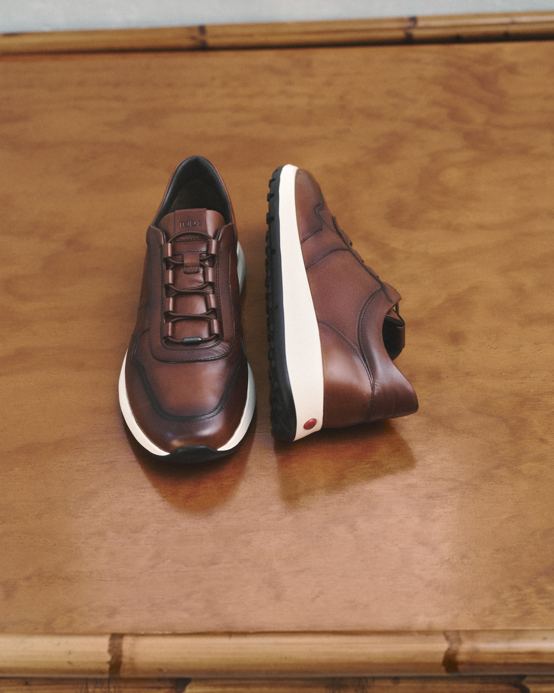 Pair of brown leather sneakers with white soles on a wooden surface.