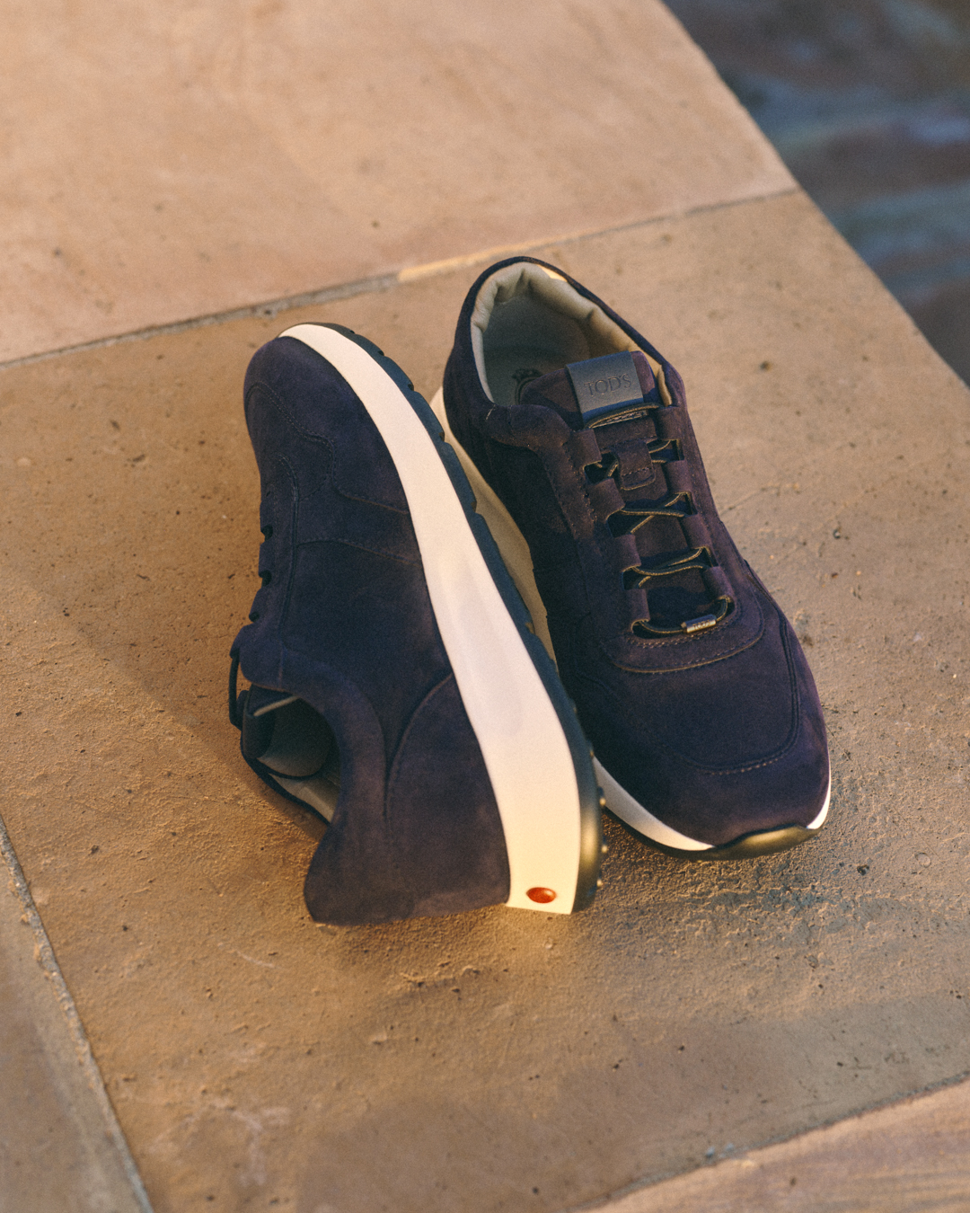 Pair of dark blue suede sneakers with white soles placed on a stone surface.