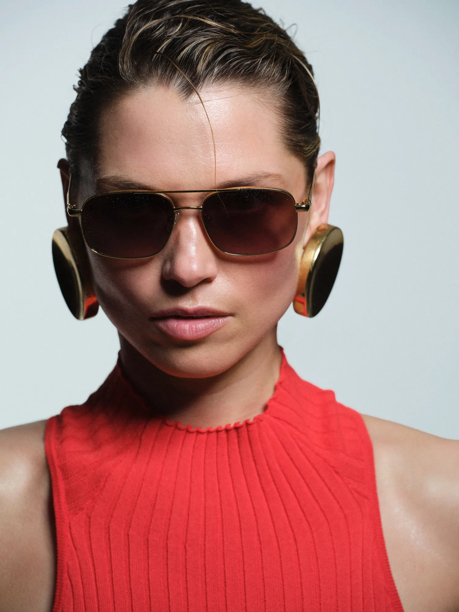 Close-up of a person wearing sunglasses, large gold earrings, and a red sleeveless top.