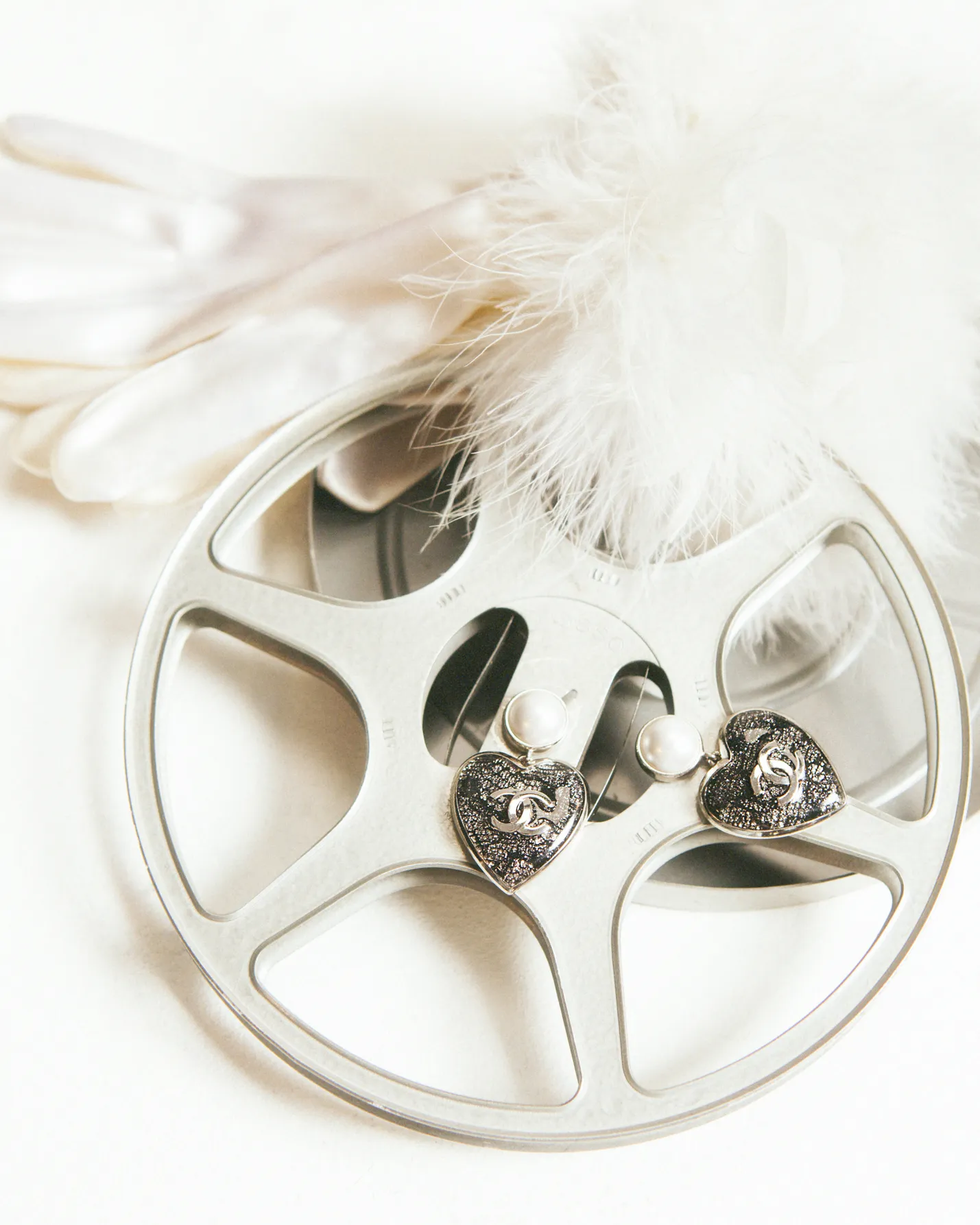 Silver film reel with pearl-topped heart-shaped Chanel earrings and white gloves with feathers.
