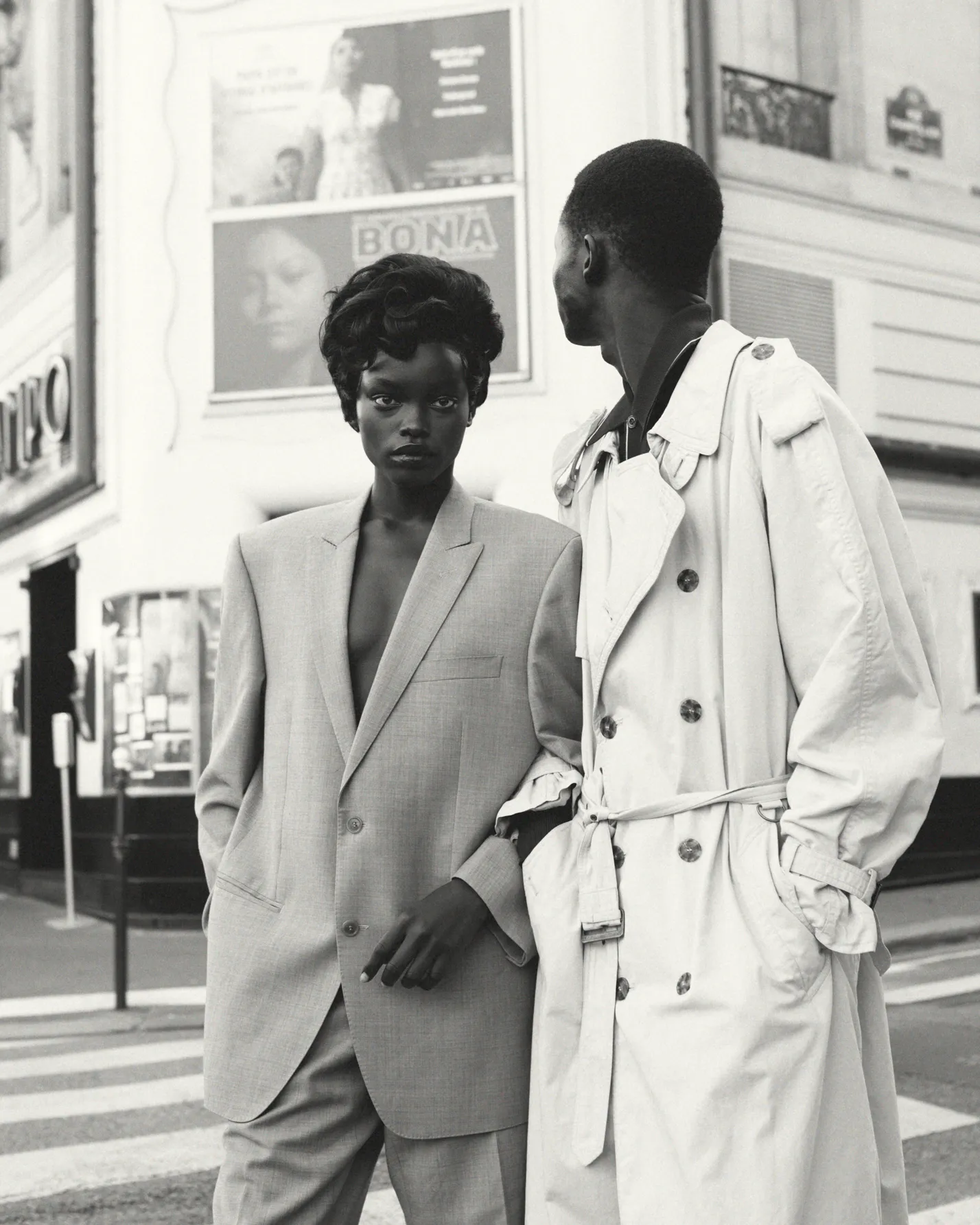 Black and white photo of two stylish people in oversized coats standing on a city crosswalk.