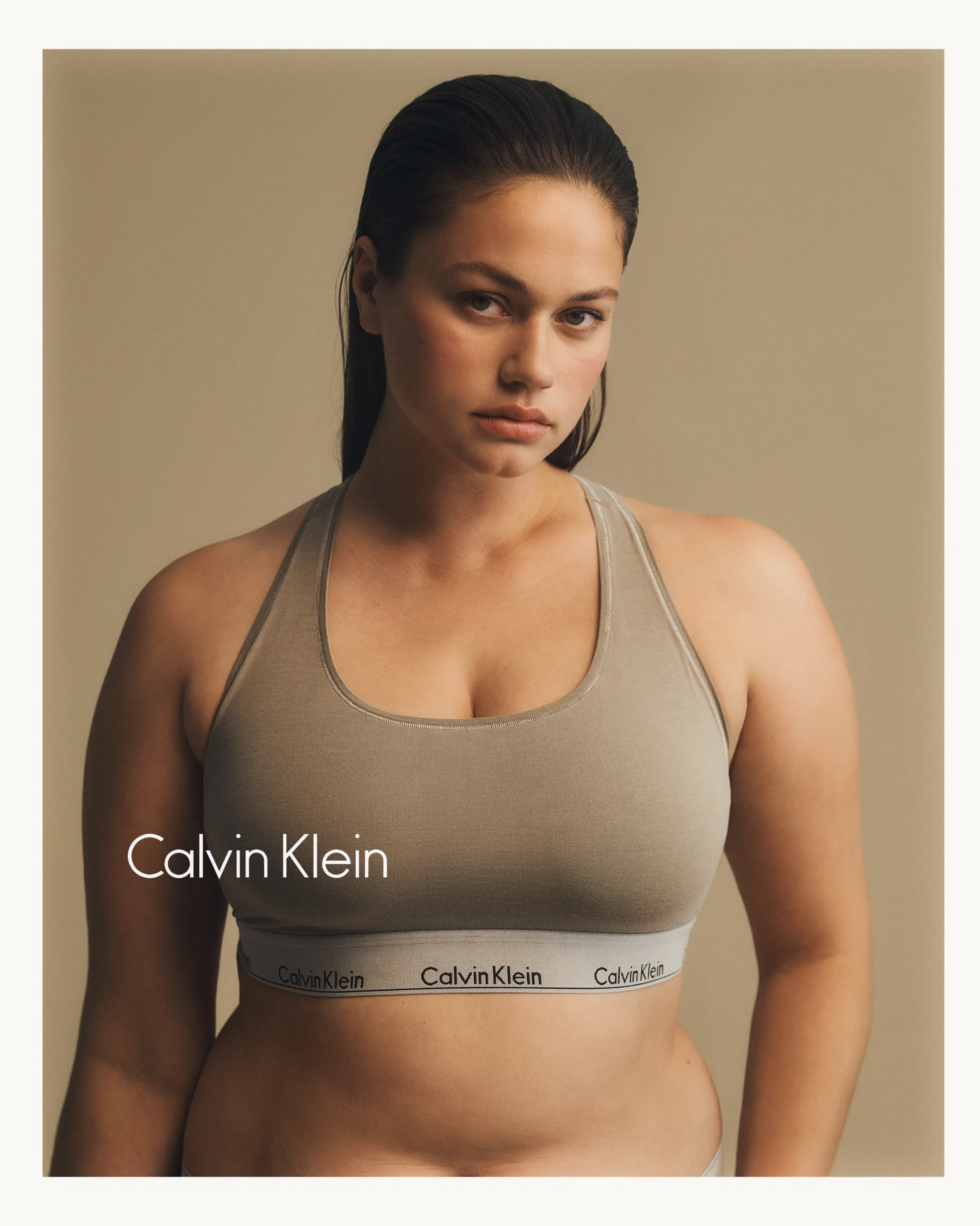Woman wearing a beige Calvin Klein sports bra against a neutral background.