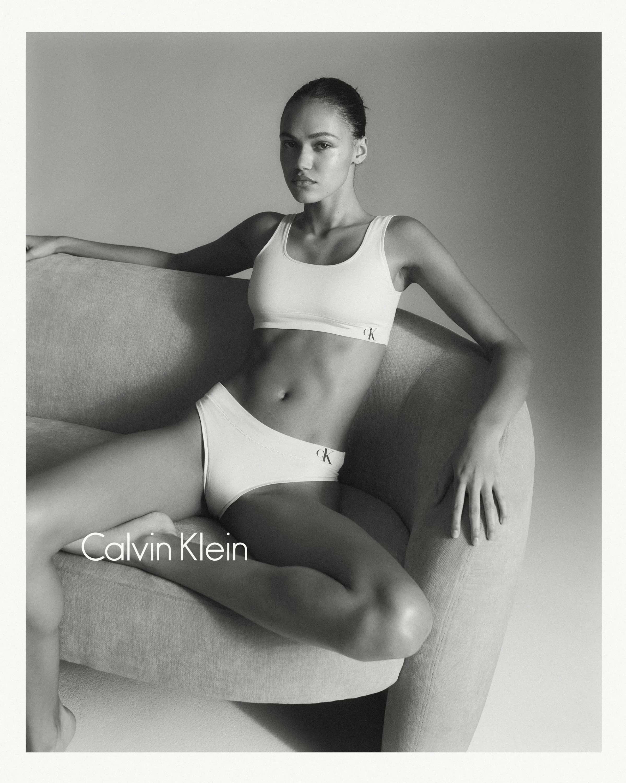Black and white photo of a woman wearing Calvin Klein white underwear lounging on a curved chair.