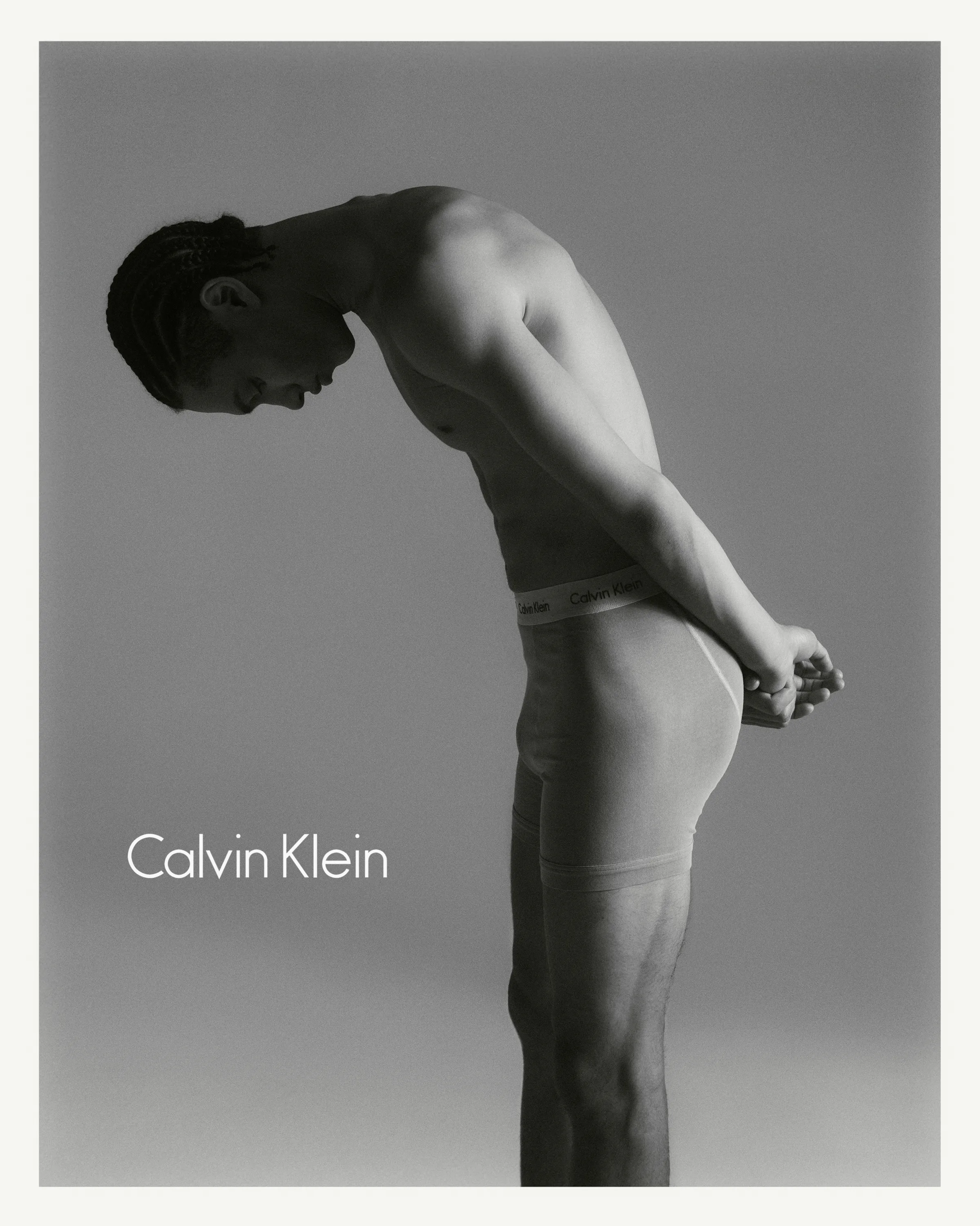 Black and white photo of a man in Calvin Klein underwear bending forward with hands behind his back.
