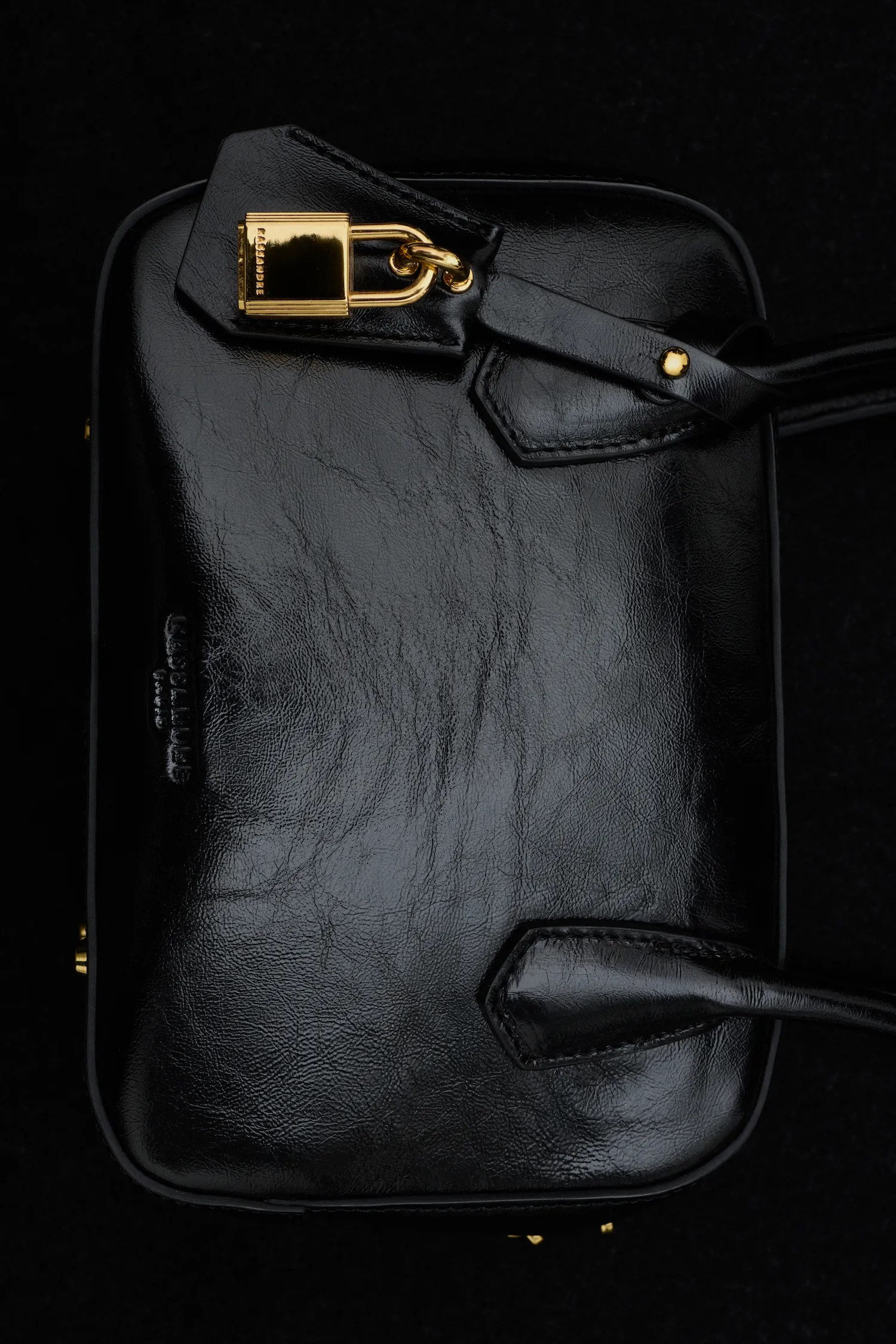 Black leather handbag with gold padlock and black handles on a black background.