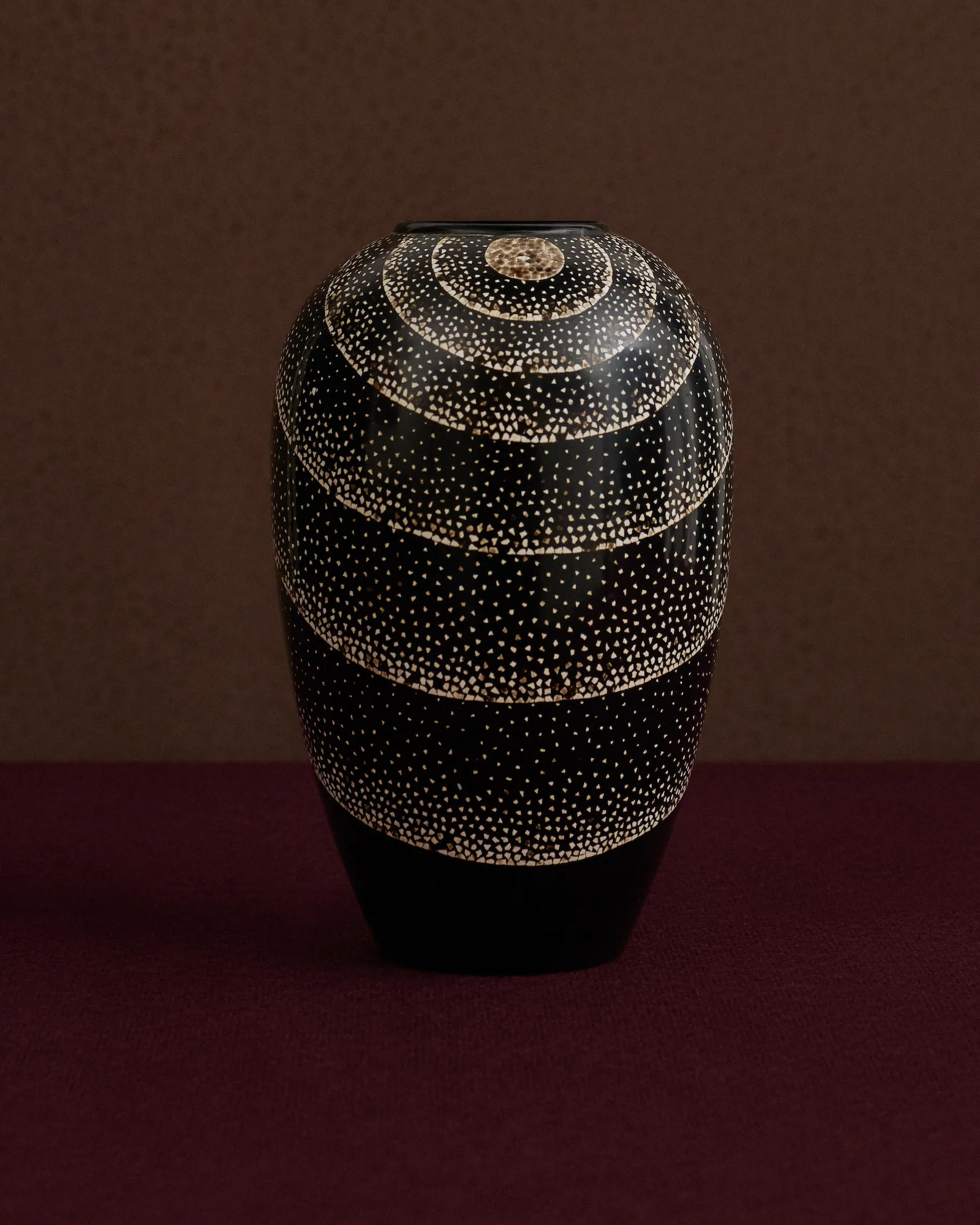 Black ceramic vase with white dotted concentric circle patterns on a dark purple surface.