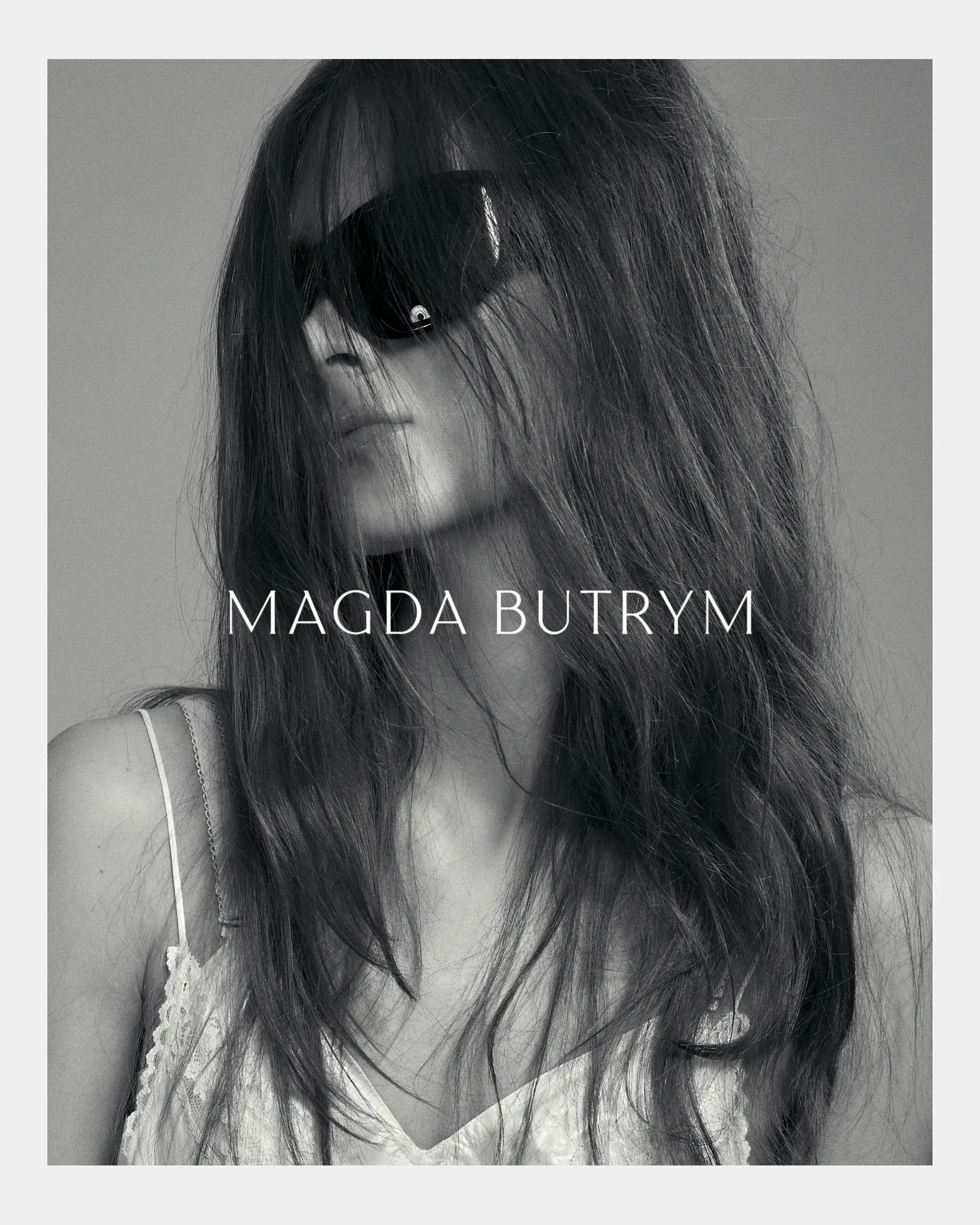 Black-and-white portrait of a woman with long hair wearing dark sunglasses and a lace-trimmed top.