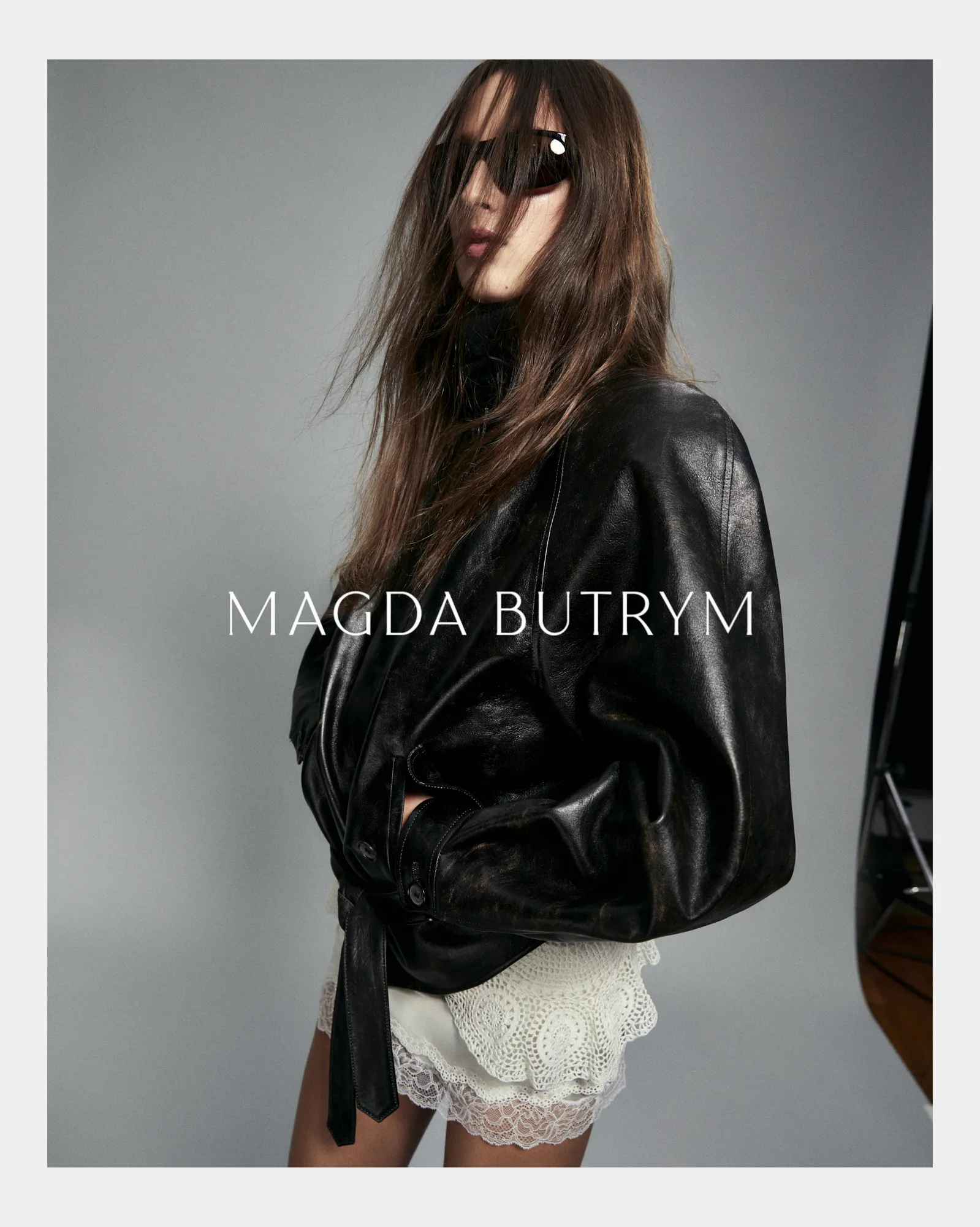 Model wearing black leather jacket and white lace skirt with long hair partially covering her face.