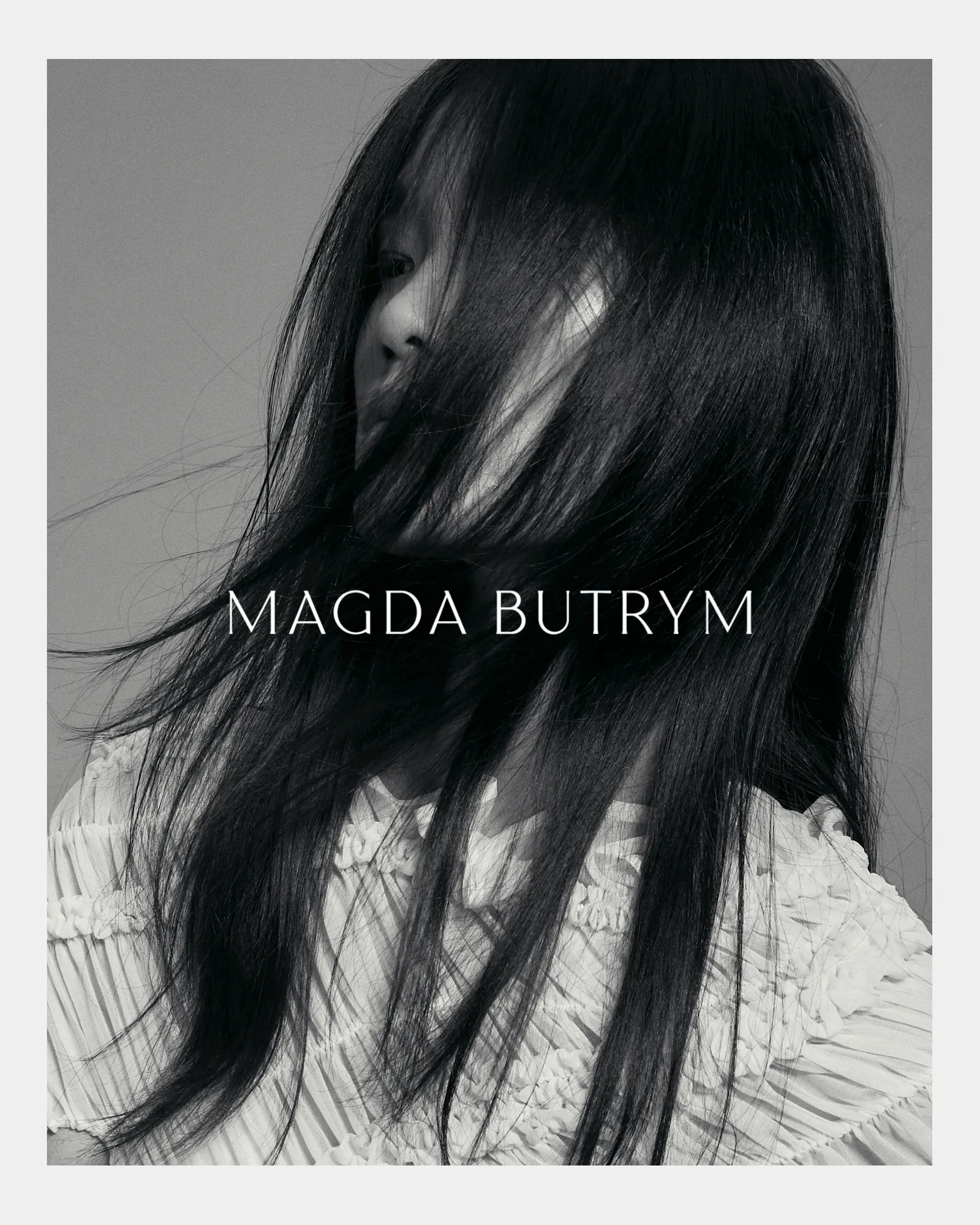 Black and white close-up of woman with long hair covering face wearing textured white blouse.
