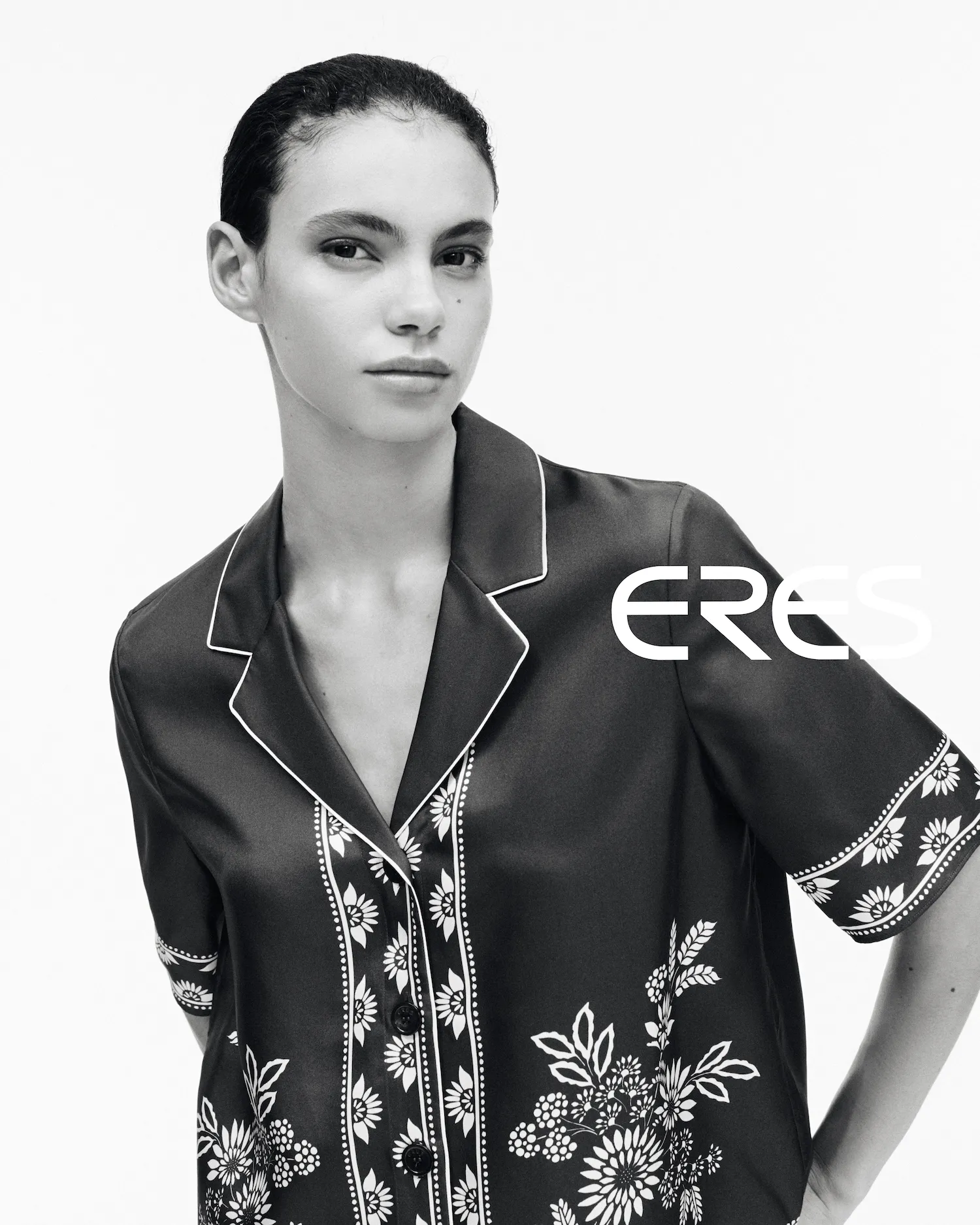 Woman with slicked-back hair wearing a dark buttoned blouse with white floral patterns.
