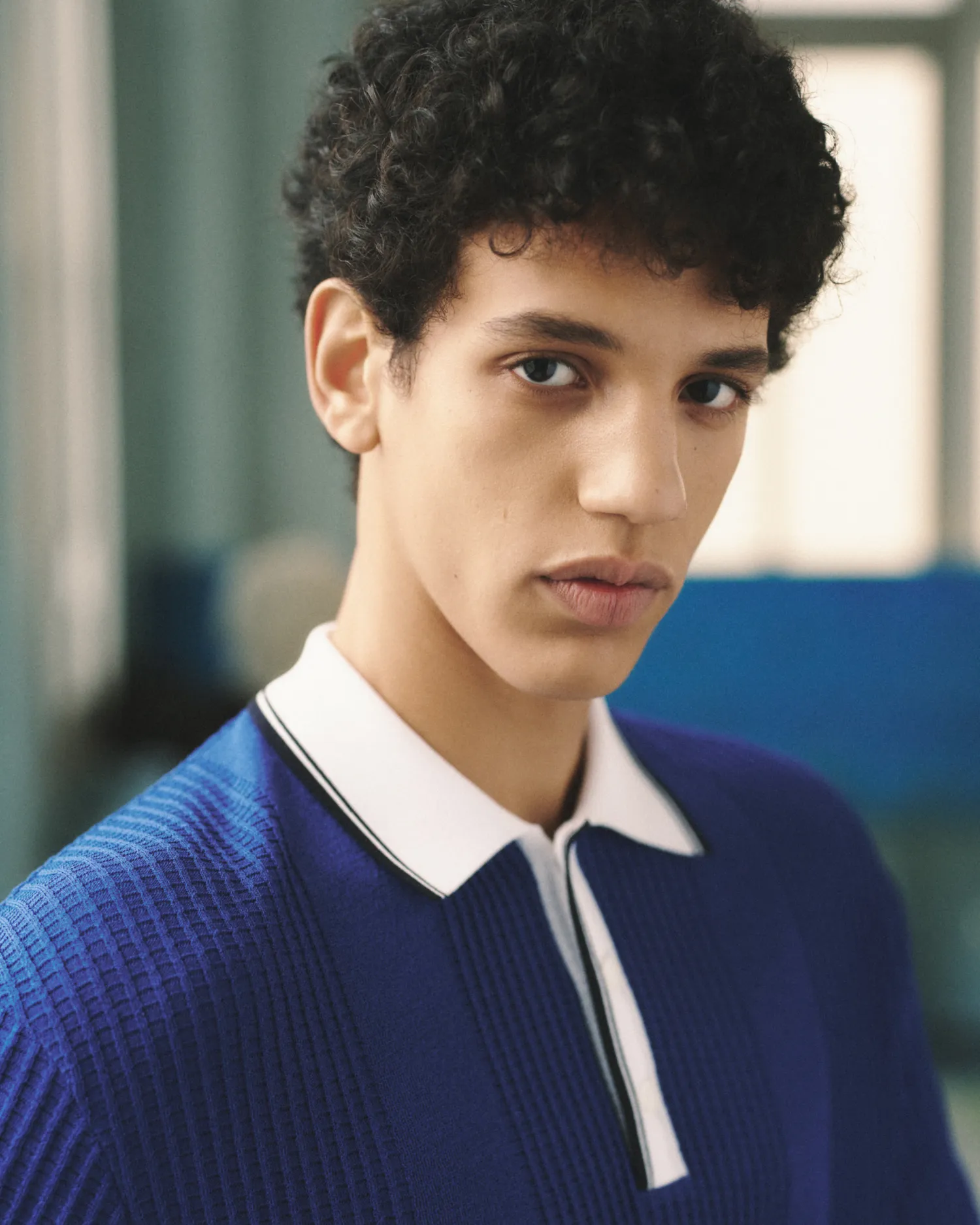 Close-up of a young man with curly hair wearing a blue shirt with a white collar.