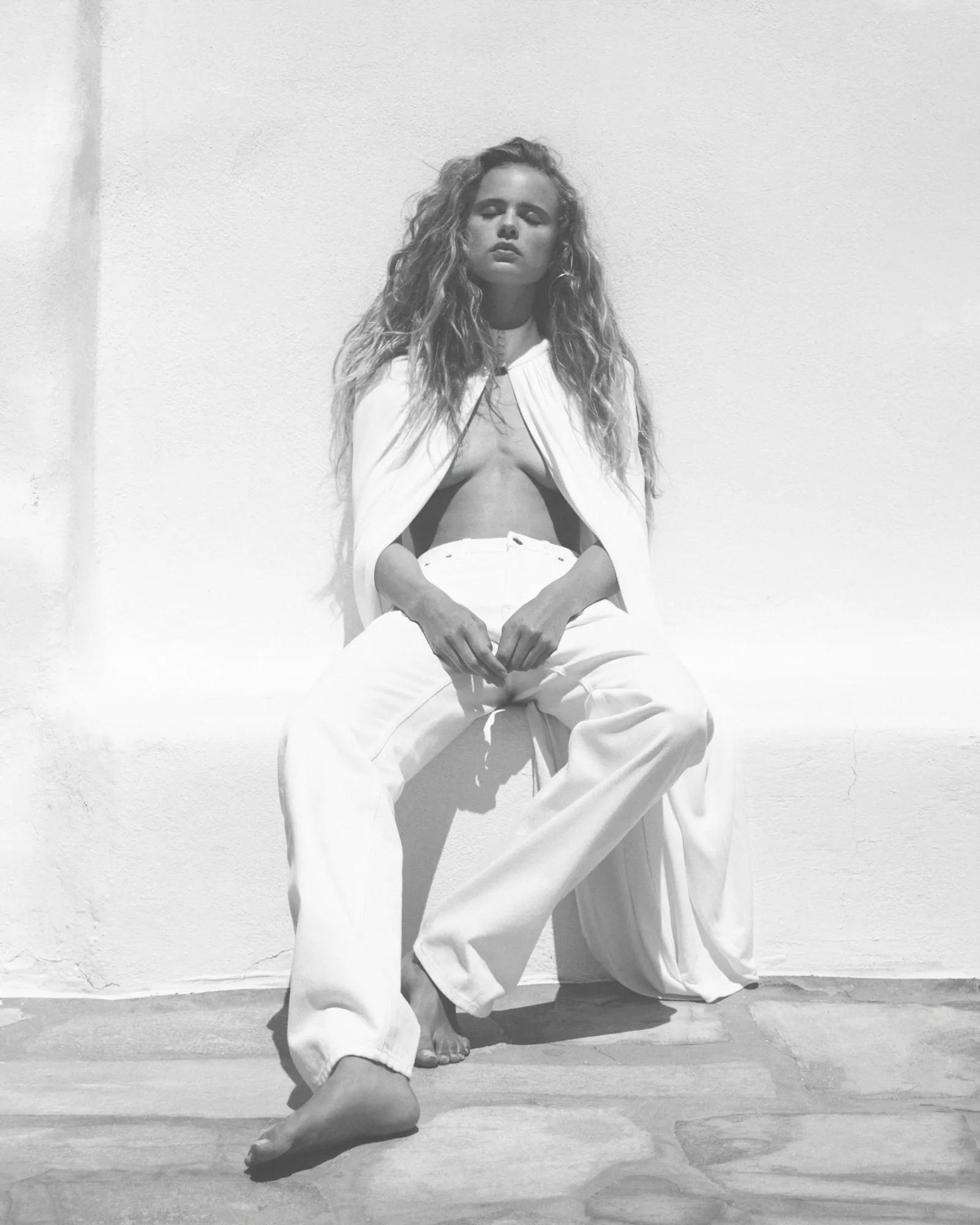 Person reclining on wooden chair outdoors with legs crossed, wearing white pants and brown shoes.