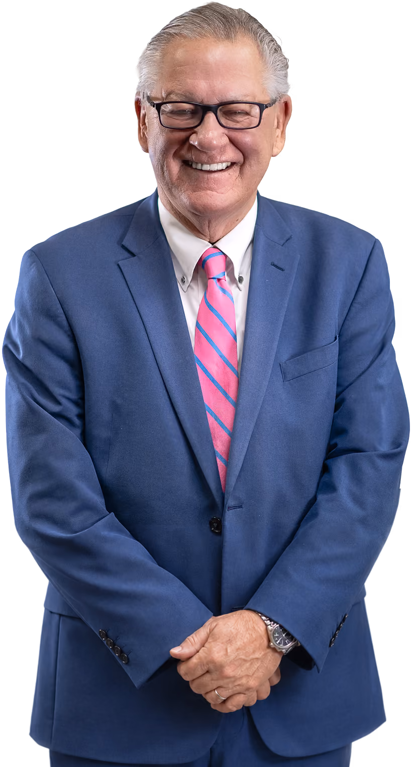Older man wearing glasses, blue suit, white shirt, and pink striped tie smiling at the camera.
