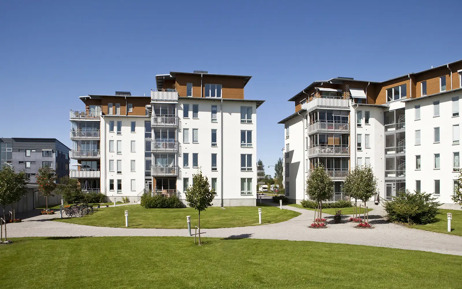 Zwei moderne Mehrfamilienhäuser mit weißen Fassaden und braunen Dachaufbauten an sonnigem Tag.