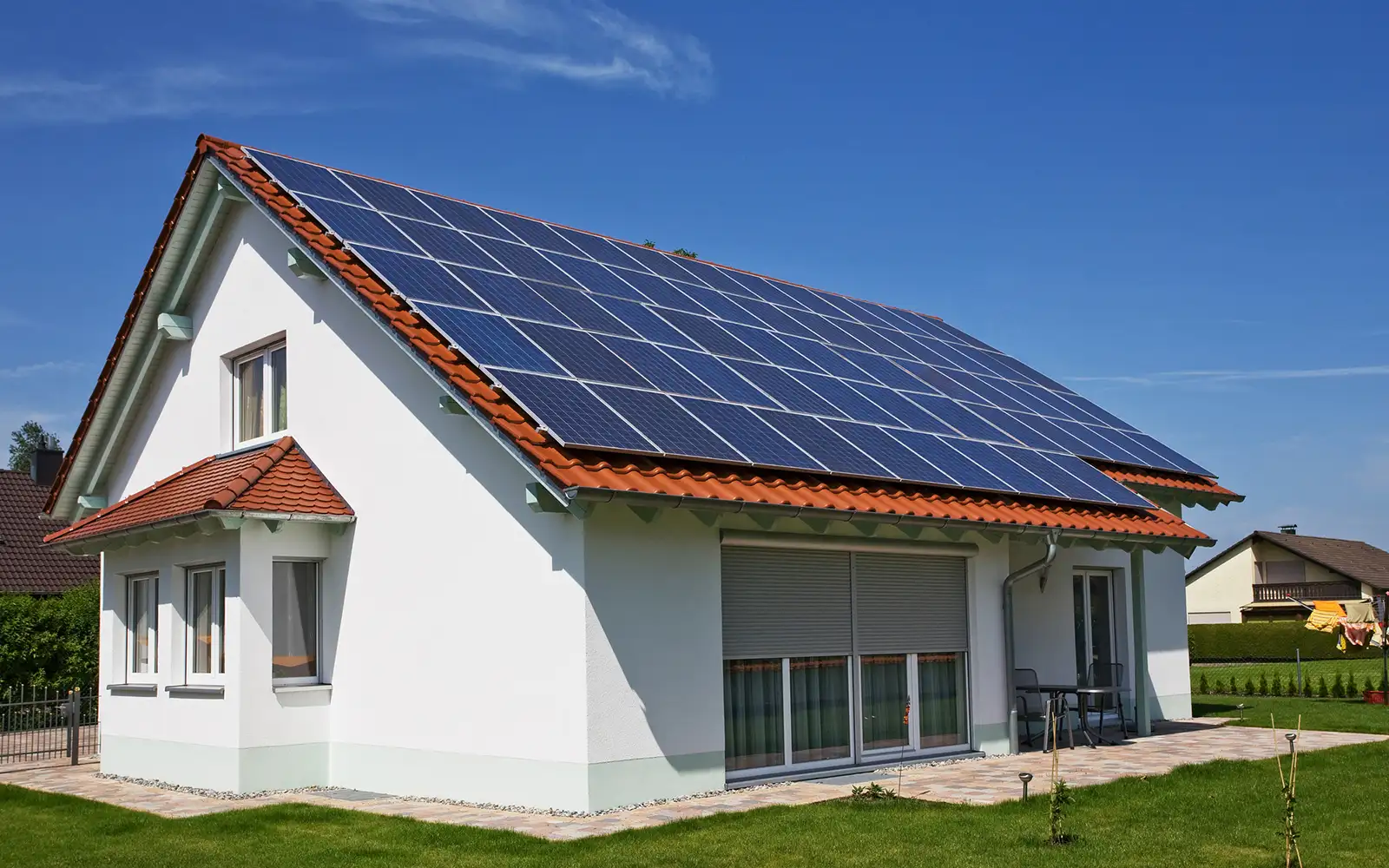 Modernes Einfamilienhaus mit weißen Wänden, roten Ziegeldach und Solarpaneelen auf dem Dach.