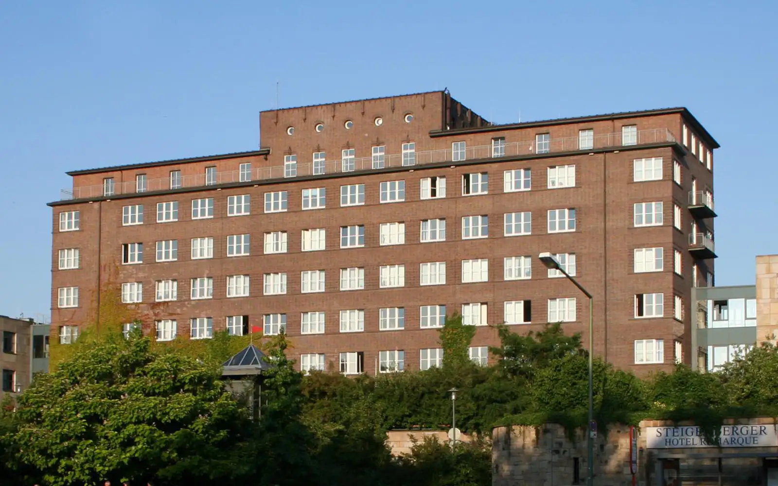 Mehrstöckiges Hotelgebäude aus rotem Backstein mit vielen Fenstern vor blauem Himmel.