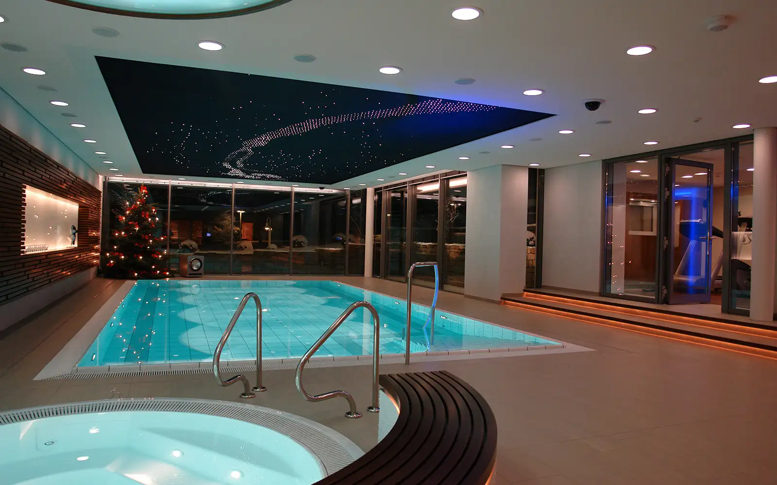 Innenpool mit Whirlpool und Weihnachtsbaum, modernes Deckenlicht und Zugang zu Fitnessbereich.