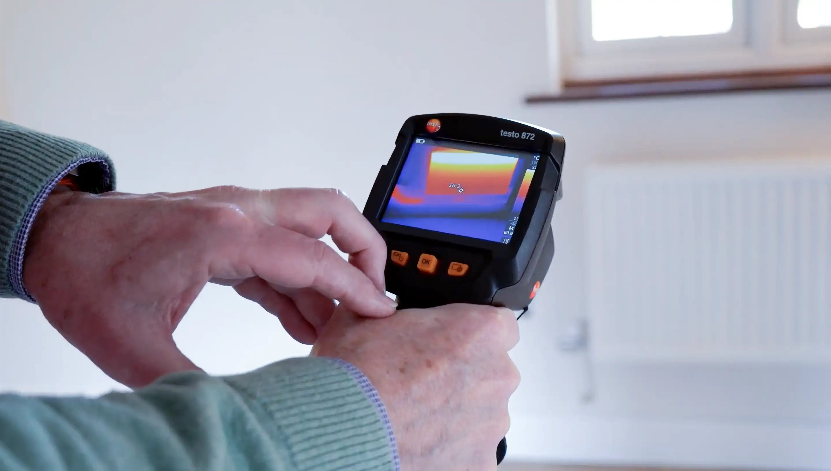 Person hält ein Thermografiegerät, das Temperaturunterschiede an einer Wand anzeigt.