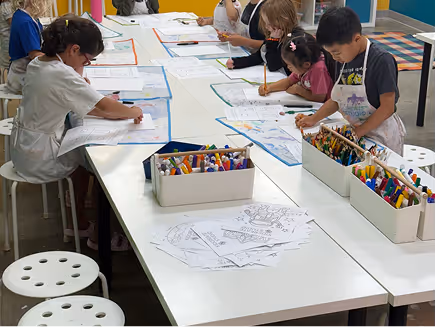 Kids gathered around studio tables drawing together in class