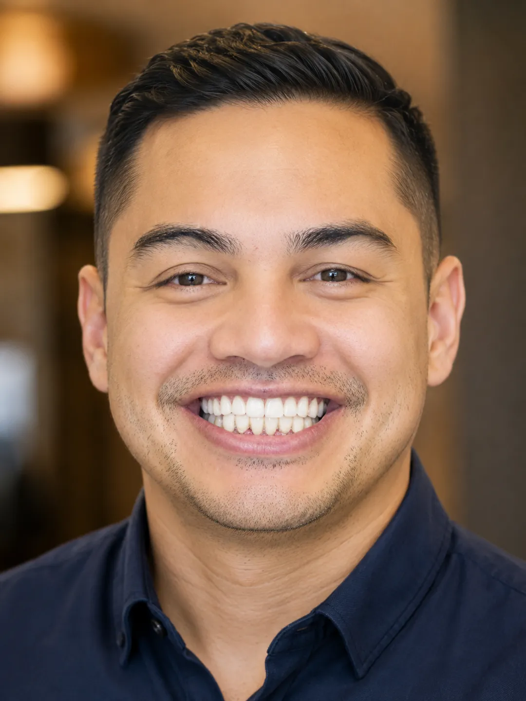 Portrait of a man smiling with short black hair and wearing a dark blue shirt.