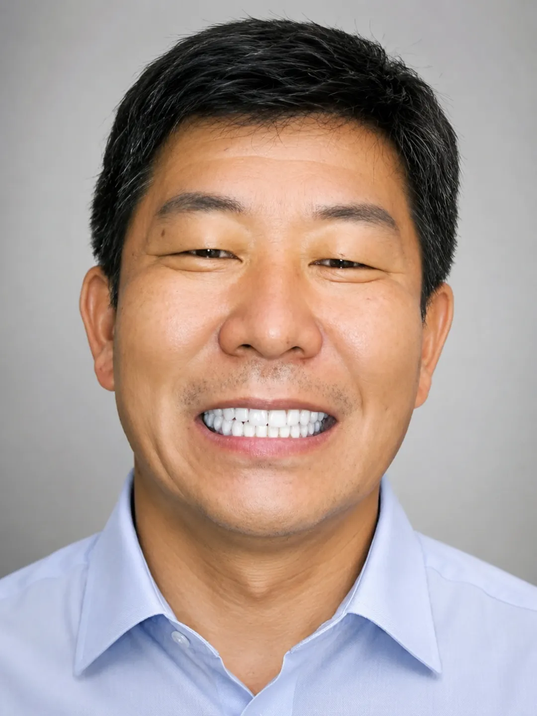Middle-aged man with black hair smiling widely, wearing a light blue button-up shirt.