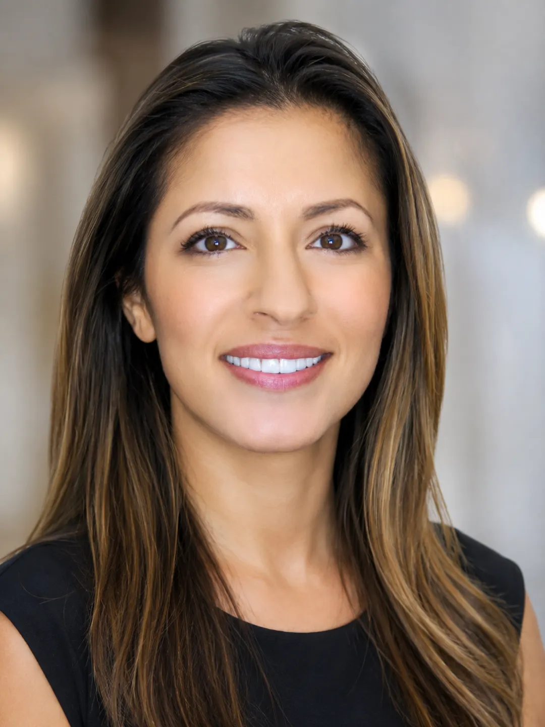 Smiling woman with long brown hair wearing a black top against a neutral background.