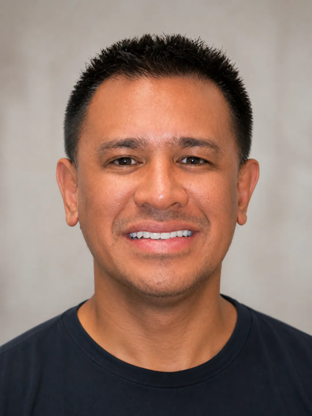 Smiling man with short black hair wearing a black crew-neck shirt against a plain background.