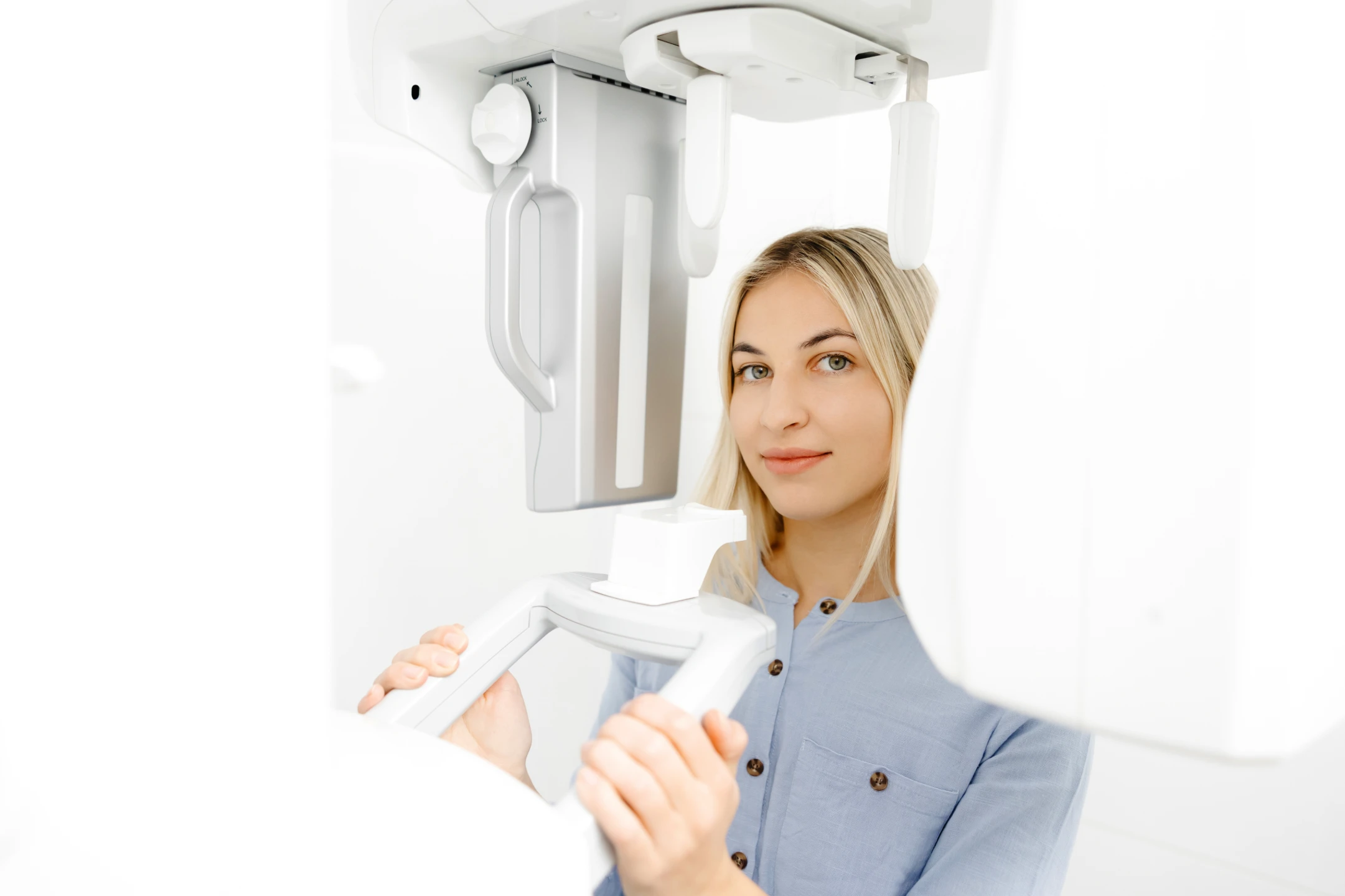 Young woman using a dental panoramic X-ray machine in a bright clinical setting.