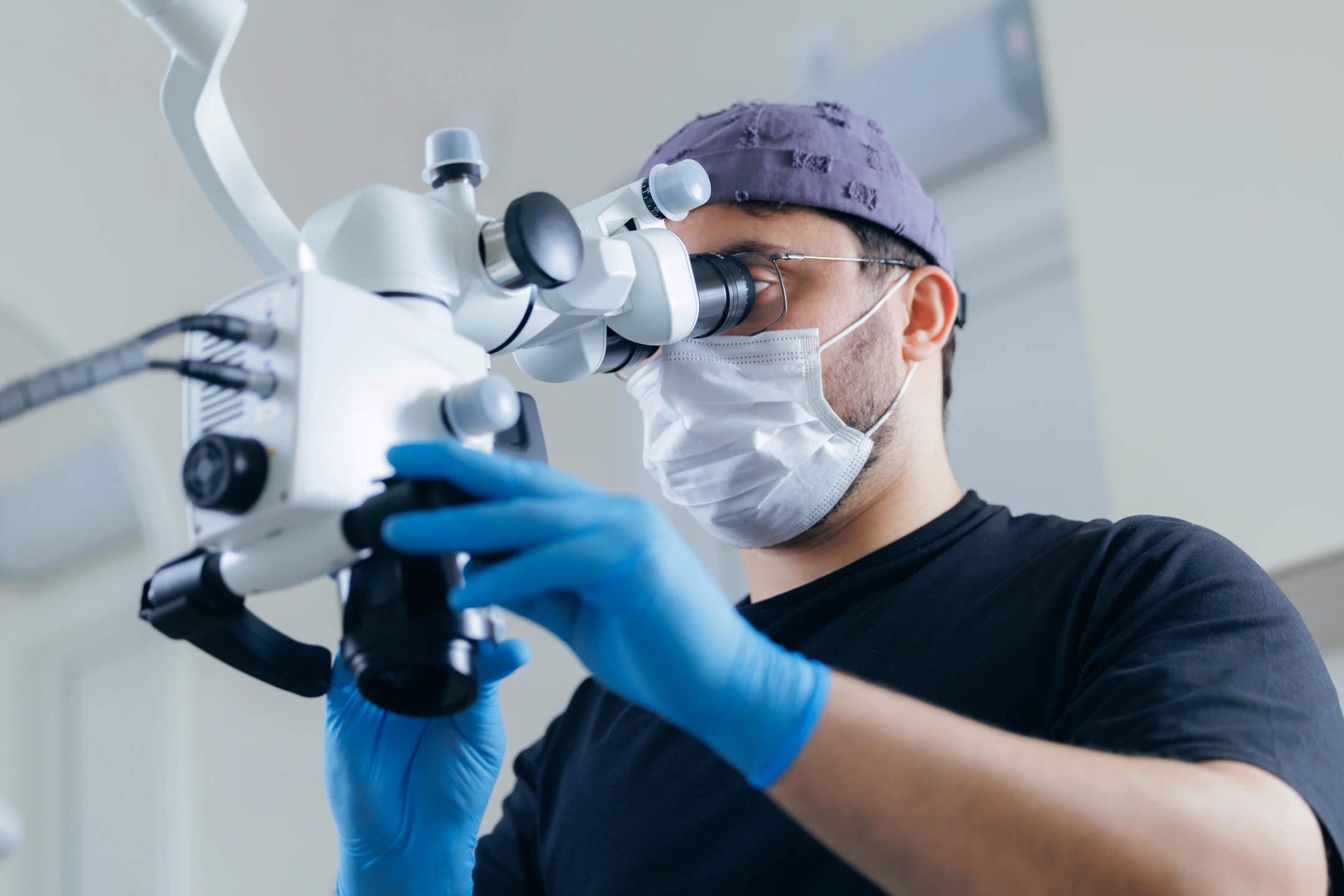 Medical professional in mask and gloves looking through a microscope in a clinical setting.