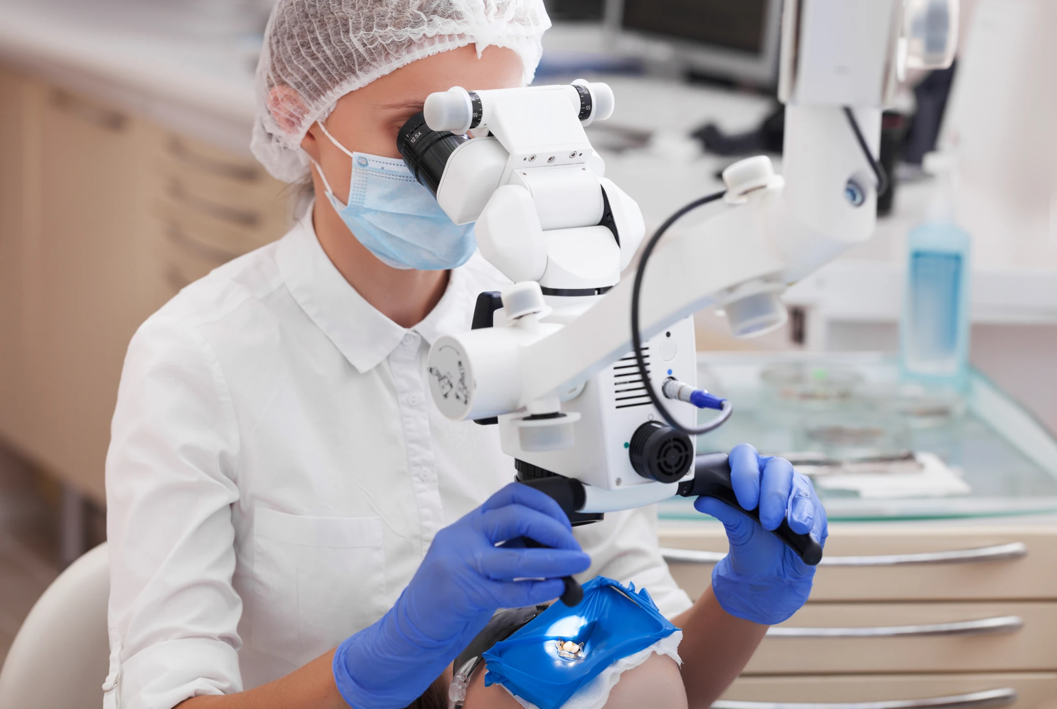 Dentist wearing mask and gloves using a microscope for a dental procedure on a patient.