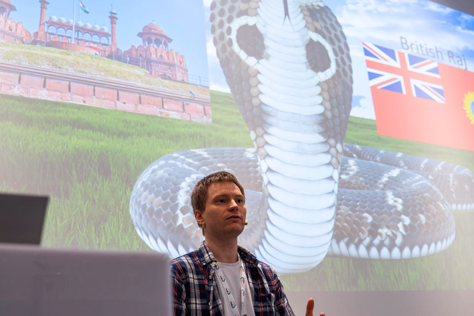 Mann med mikrofon foran et stort bilde av en kobra og en historisk bygning i bakgrunnen.