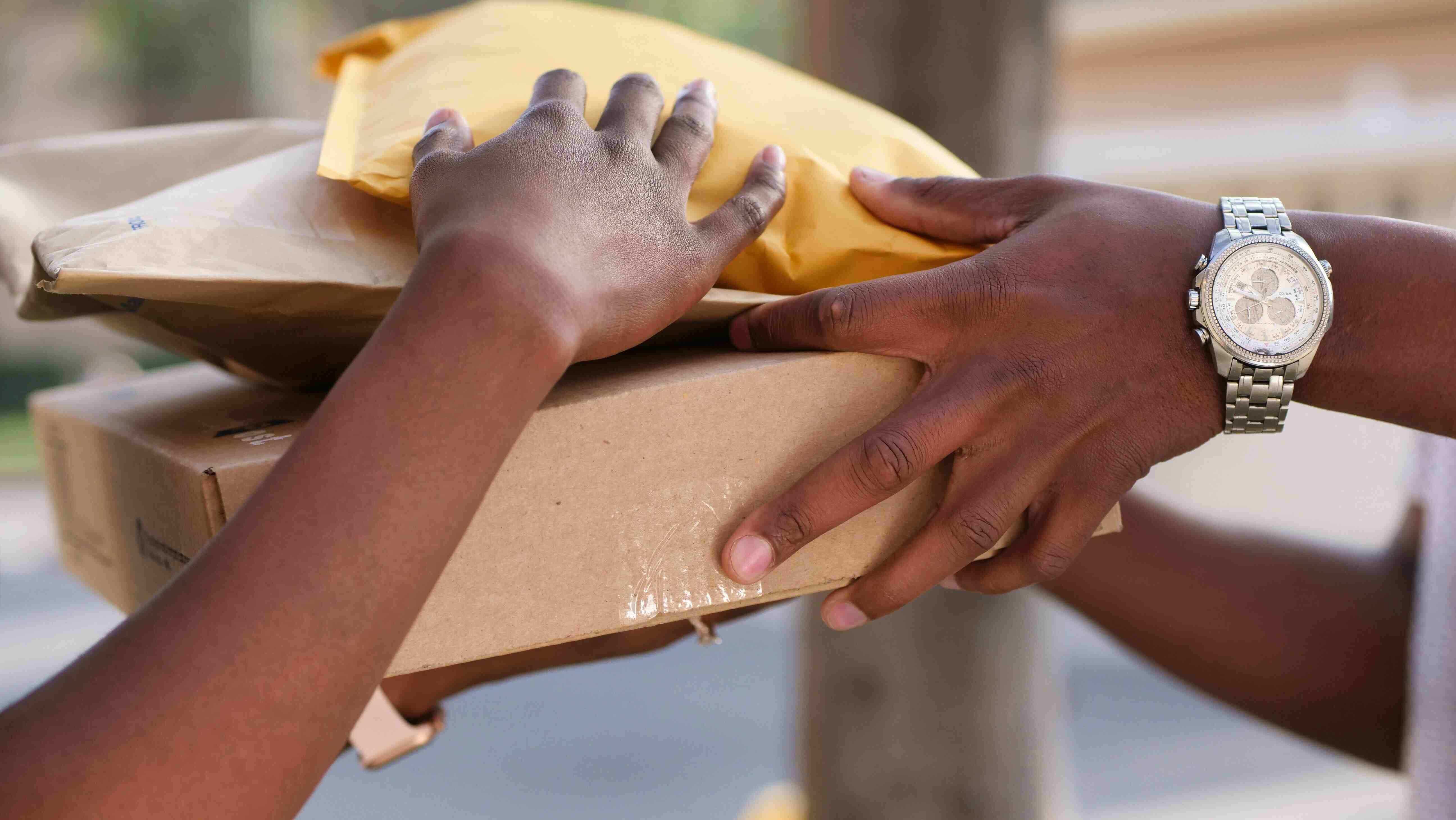 Dos pares de manos sostienen a la vez una caja de cartón y dos sobres acolchados en el momento de la entrega