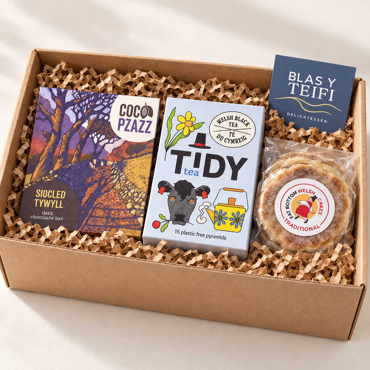 Example Blas y Teifi welcome hamper with Tidy Tea, Coco Pzazz chocolate and Fat Bottom Welsh Cakes in a kraft gift box.