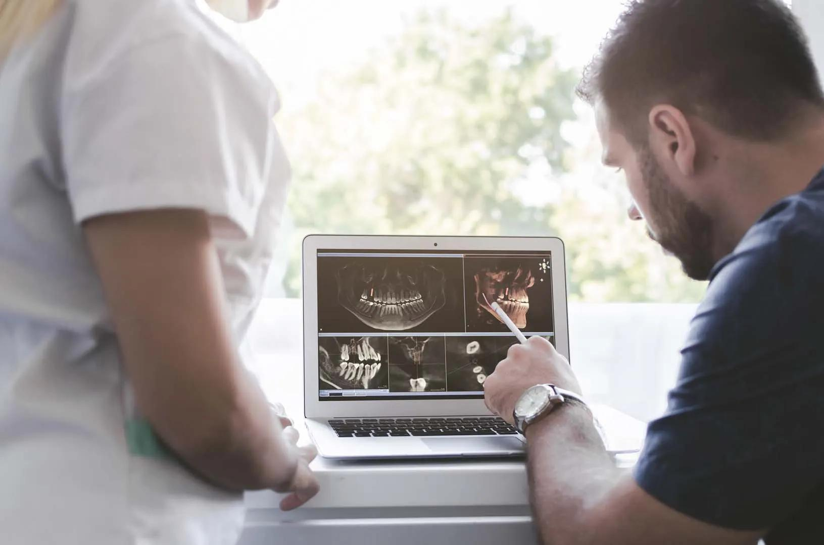 Two dental professionals reviewing jaw and teeth X-ray images on a laptop computer.
