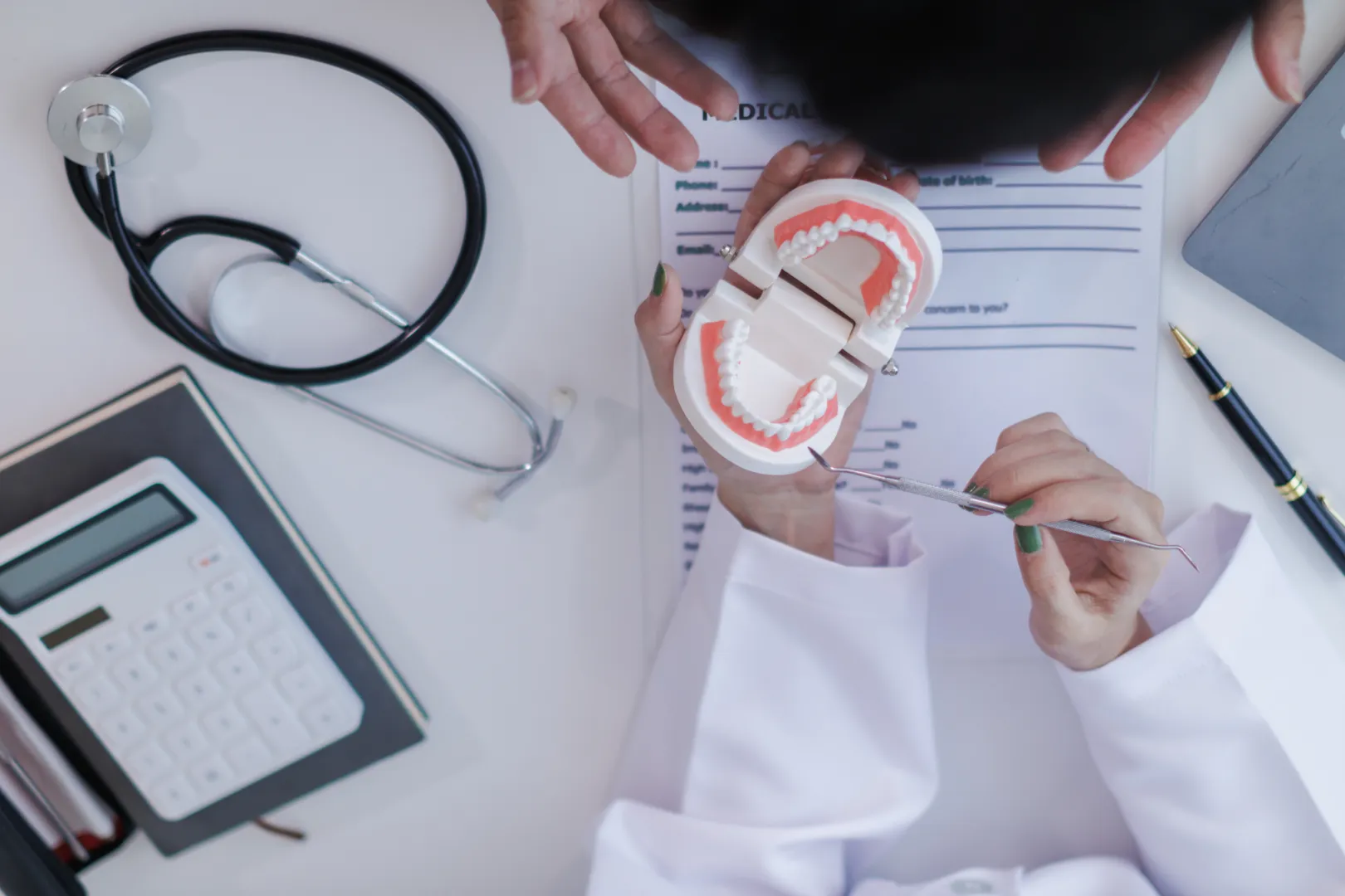 Dentist showing a dental model and tool to a patient over a desk with medical items.
